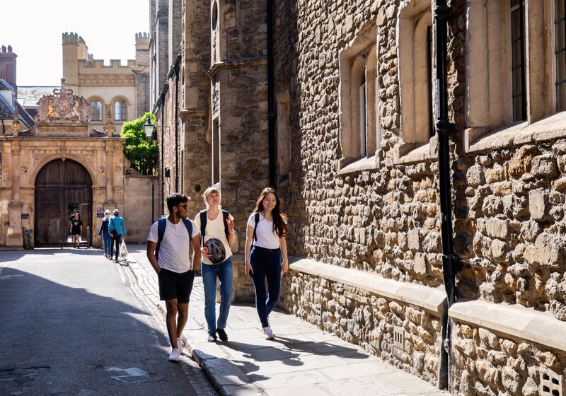 Three University of Cambridge students walking on Trinity Lane in sunshine.